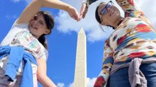 Mother and daughter standing with arms creating a heart shape. Washington Monument can be seen through the heart shape created by their arms.